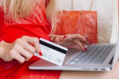 woman-red-sitting-with-laptop-card-near-shopping-bags